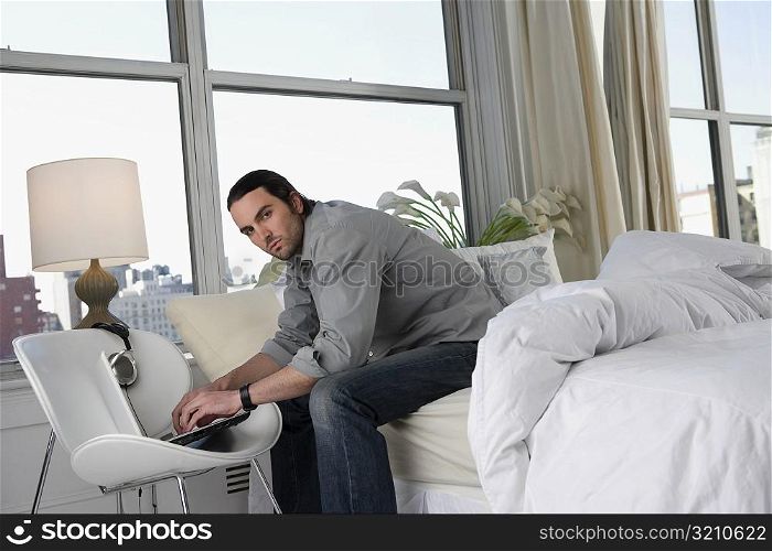 Portrait of a young man sitting on the bed and working on a laptop