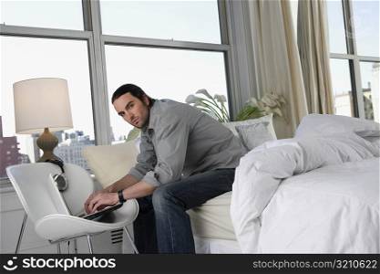 Portrait of a young man sitting on the bed and working on a laptop