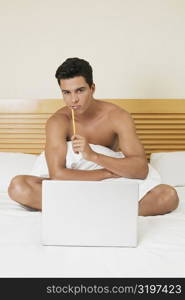 Portrait of a young man sitting on the bed with a laptop