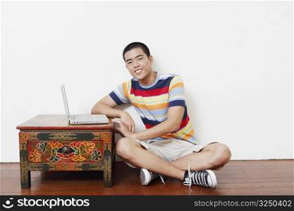 Portrait of a young man sitting on the floor with a laptop on the table