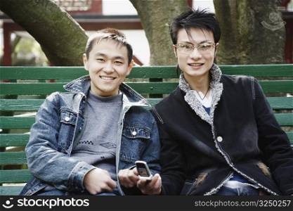 Portrait of a young man sitting together with his friend holding a mobile phone