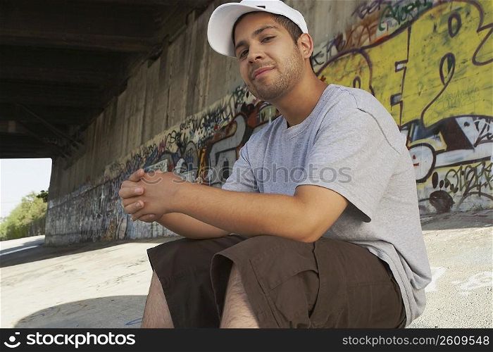 Portrait of a young man sitting under a bridge