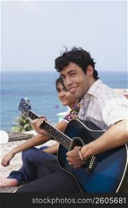 Portrait of a young man sitting with a young woman and playing a guitar