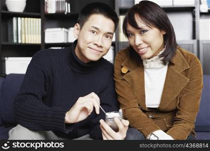 Portrait of a young man sitting with a young woman on a couch holding a mobile phone