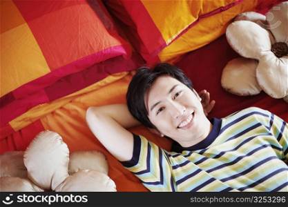 Portrait of a young man smiling and lying on the bed with his hand behind his head