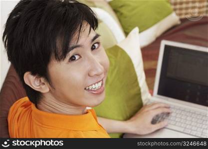 Portrait of a young man smiling and using a laptop