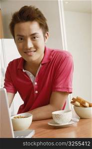 Portrait of a young man smiling in front of a laptop at a kitchen counter