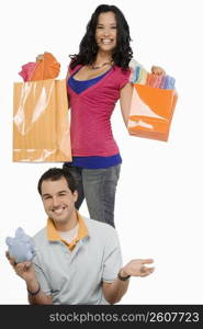 Portrait of a young man smiling with a young woman standing behind him holding shopping bags