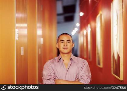 Portrait of a young man standing in a corridor with his arms crossed
