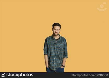 Portrait of a young man standing with hands in pockets over colored background