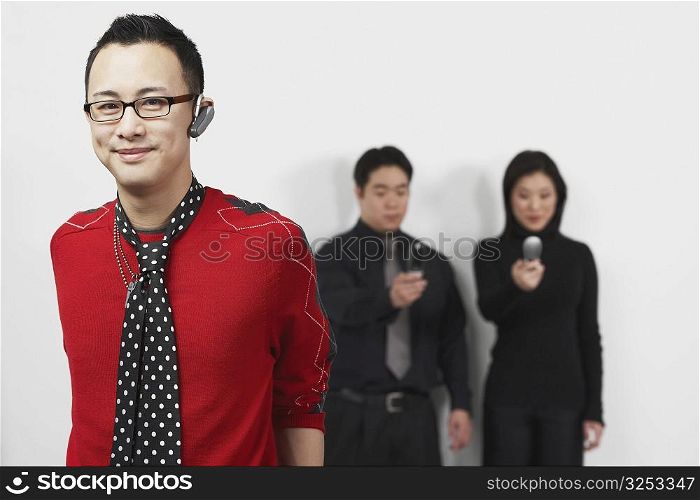 Portrait of a young man using a hands free device with a businessman and businesswoman standing behind him