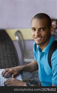 Portrait of a young man using a laptop in a cafe and smiling
