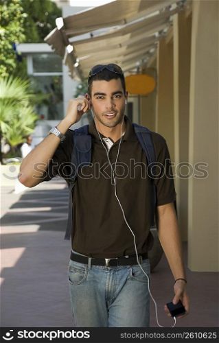 Portrait of a young man walking and listening to an MP3 player