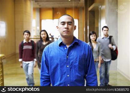 Portrait of a young man walking in the corridor with four people behind him