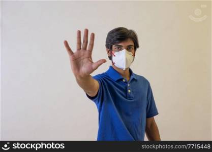 Portrait of a young man wearing a face mask signalling stop sign with hand.