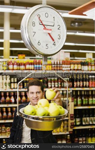 Portrait of a young man weighing apples on a weighing scale in a supermarket
