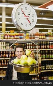 Portrait of a young man weighing apples on a weighing scale in a supermarket