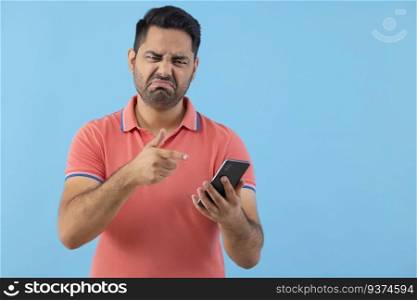 Portrait of a young man with displeased facial expression pointing at his Smartphone