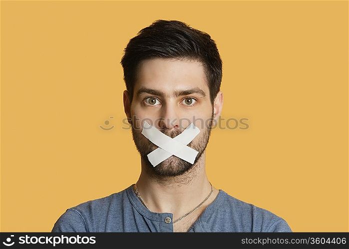 Portrait of a young man with tape on mouth over colored background