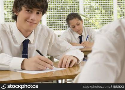 Portrait of a young man writing on paper sheet and smiling with a teenage girl behind him