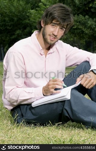 Portrait of a young man writing with a pen on a notepad