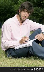 Portrait of a young man writing with a pen on a notepad