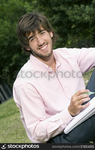 Portrait of a young man writing with a pen on a notepad and smiling