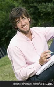 Portrait of a young man writing with a pen on a notepad and smiling