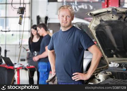 Portrait of a young mechanic in auto repair shop with customer in background