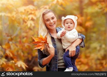 Portrait of a young mother with little baby having fun in autumn park, enjoying beauty of fall nature, happy family life
