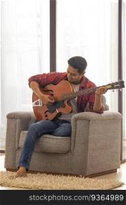 Portrait of a young musician playing guitar in living room