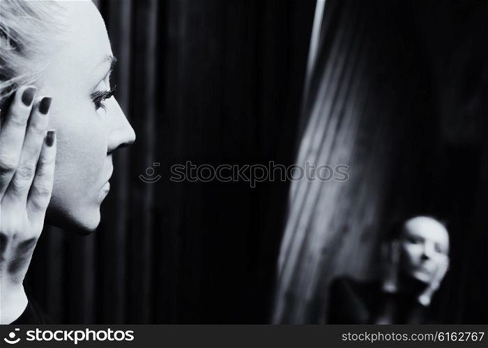 Portrait of a young sad woman looking in the mirror