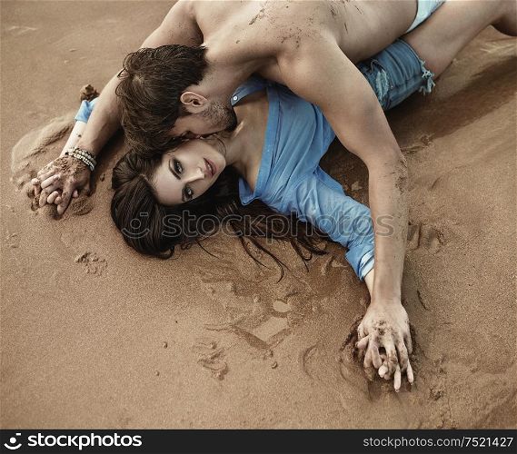 Portrait of a young sensual couple laying on the bright sand