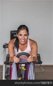 Portrait of a young sportswoman looking at camera in sportwear workout on exercise bike at gym. Front view of a young sportswoman in sportwear workout on exercise bike at gym