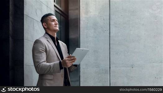 Portrait of a Young Striving CEO or Leader Working on Tablet. Businessman Standing at the City and Looking away