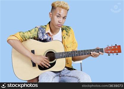Portrait of a young teenage boy playing guitar over blue background