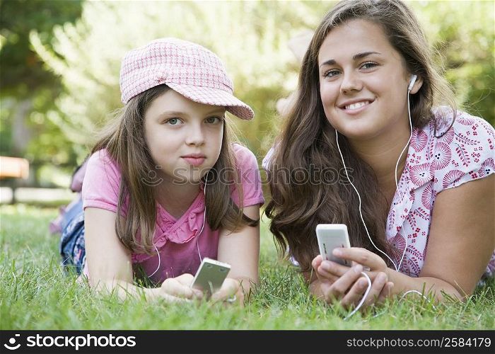 Portrait of a young woman and a girl lying on grass in a park and listening to MP3 players