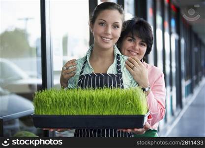 Portrait of a young woman and her mother standing with a tray of wheatgrass and smiling