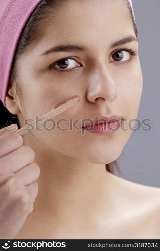 Portrait of a young woman applying a facial mask