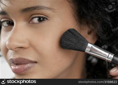 Portrait of a young woman applying blush with a brush