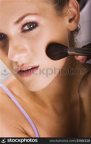 Portrait of a young woman applying blush with a brush
