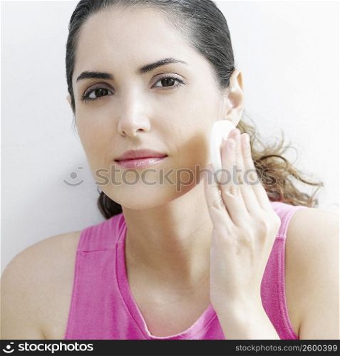 Portrait of a young woman applying face powder on her cheeks