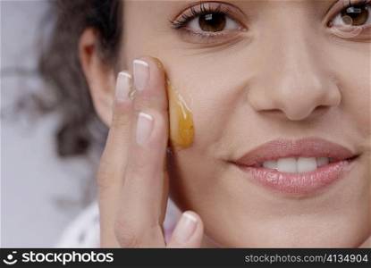 Portrait of a young woman applying honey on her cheek