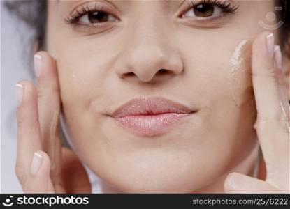 Portrait of a young woman applying moisturizer on her cheeks
