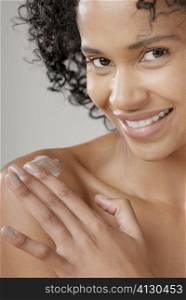 Portrait of a young woman applying moisturizer on her shoulder and smiling