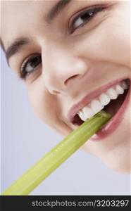 Portrait of a young woman biting into a celery stick