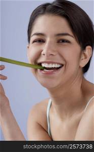 Portrait of a young woman biting into a celery stick and smiling