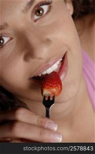 Portrait of a young woman biting into a strawberry with a fork
