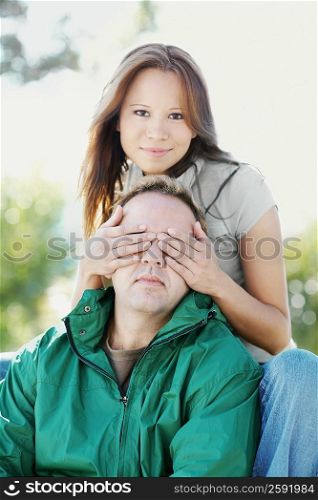 Portrait of a young woman covering a mid adult man&acute;s eyes