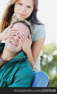 Portrait of a young woman covering a mid adult man&acute;s eyes